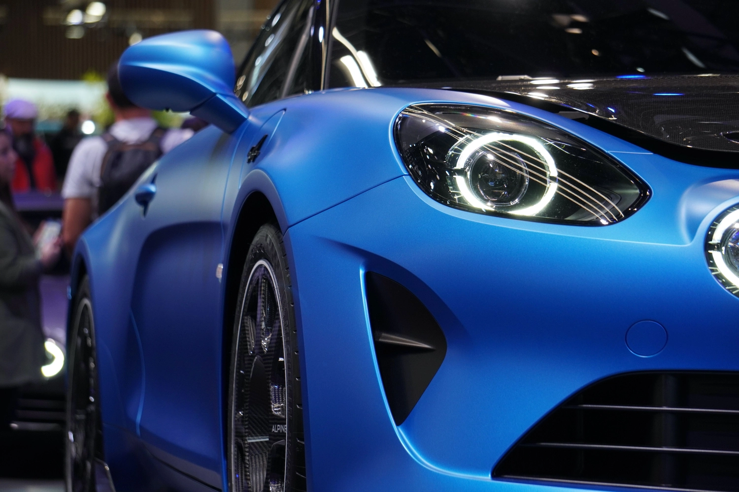 Digitaleanmeldung - Kfz Zulassungsdienst - Nahaufnahme eines mattblauen Alpine A110 Sportwagens, die den markanten runden LED-Scheinwerfer und den eleganten vorderen Kotflügel hervorhebt.